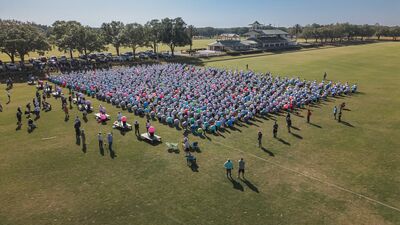 A large crowd participating in a cardio drumming event on a polo field